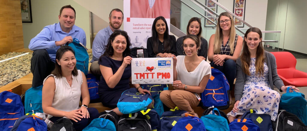Employees pose with donated backpacks and school supplies for underserved OC students.