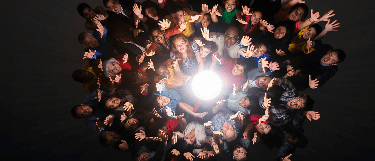 Group Of People In A Dark Room With Their Hands Up Near A Light